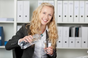Portrait of happy businesswoman pouring water in glass from bottle at office